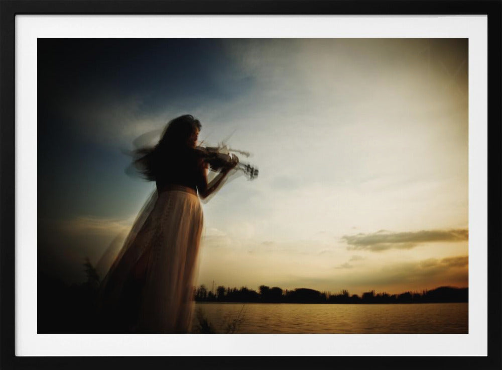 An artistic, framed photograph with motion blur capturing the silhouette of a woman in a long flowing skirt playing the violin by a lake against a dramatic sunset sky. Poster