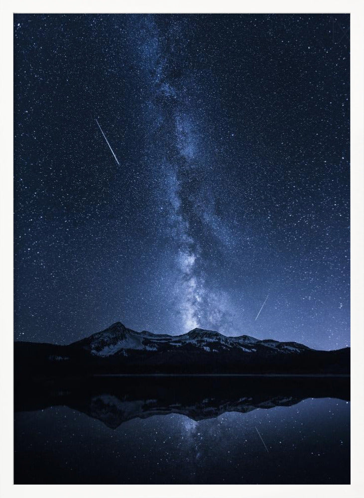 A breathtaking night photograph of the Milky Way galaxy stretching vertically across a deep blue, star-filled sky. Two shooting stars streak through the atmosphere above a dark, snow-dusted mountain range, which is perfectly reflected in the calm, mirror-like surface of a lake in the foreground. Artwork