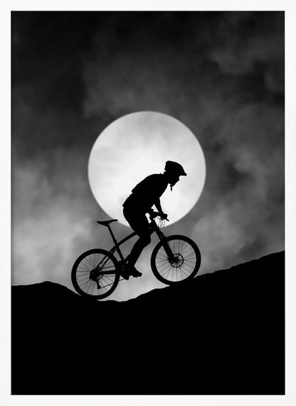 A dramatic black and white silhouette of a mountain biker riding uphill against the backdrop of a large, full moon in a cloudy night sky. Decor