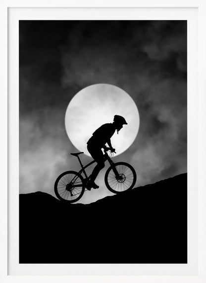 A dramatic black and white silhouette of a mountain biker riding uphill against the backdrop of a large, full moon in a cloudy night sky. Decor