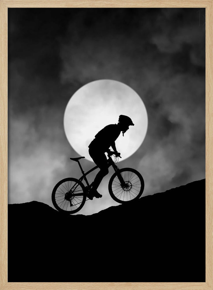 A dramatic black and white silhouette of a mountain biker riding uphill against the backdrop of a large, full moon in a cloudy night sky. Decor