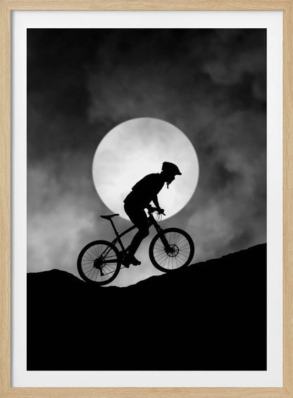 A dramatic black and white silhouette of a mountain biker riding uphill against the backdrop of a large, full moon in a cloudy night sky. Decor