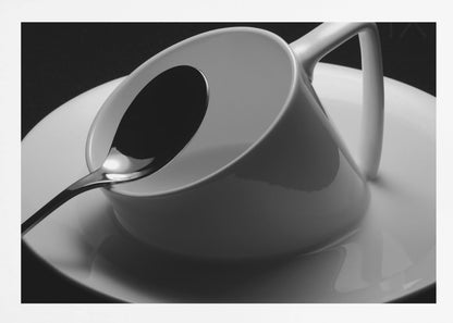 A dramatic black and white close-up photograph of a white porcelain coffee cup tilted on its saucer, with a reflective spoon resting inside. The image has high contrast against a dark background and is presented within a silver-colored frame. Decor