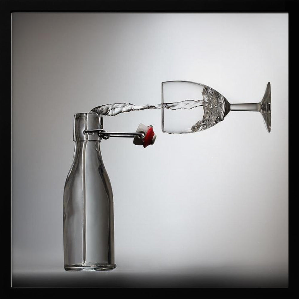 A conceptual photograph in a light wood frame depicting water pouring horizontally from an open swing-top glass bottle into a floating, sideways wine glass against a simple gray background, capturing the liquid in mid-air. Print