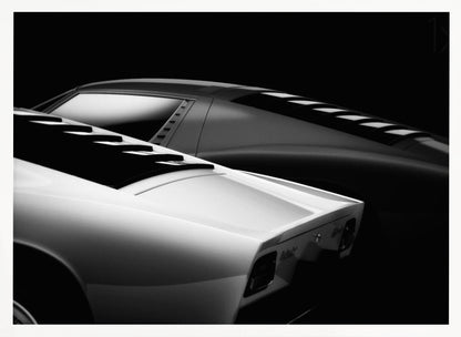 A dramatic black and white studio photograph showcasing the sleek, curved lines of two classic sports cars, with a white car in the foreground and a dark one in the background, set against a black backdrop. Wall Art