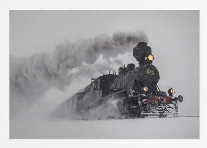 A dramatic black and white photograph of a classic steam train, number 1136, plowing through a heavy snowstorm, with its headlights glowing and a large plume of smoke trailing behind it. The image is presented within a silver frame. Print