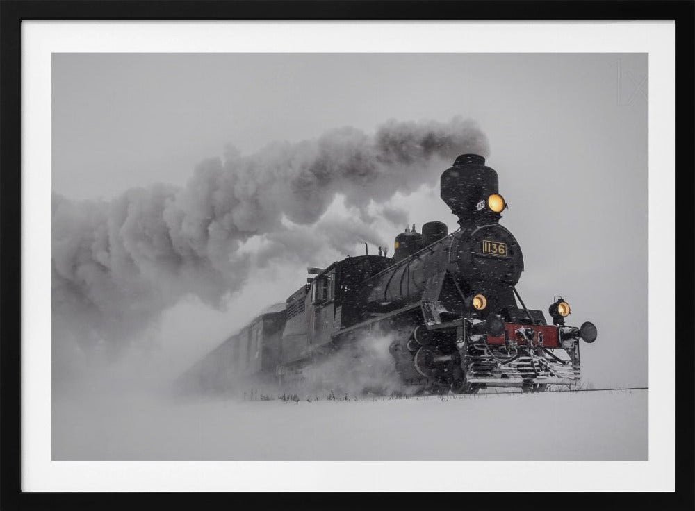 A dramatic black and white photograph of a classic steam train, number 1136, plowing through a heavy snowstorm, with its headlights glowing and a large plume of smoke trailing behind it. The image is presented within a silver frame. Print