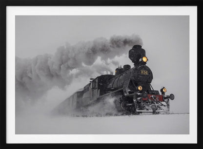 A dramatic black and white photograph of a classic steam train, number 1136, plowing through a heavy snowstorm, with its headlights glowing and a large plume of smoke trailing behind it. The image is presented within a silver frame. Print