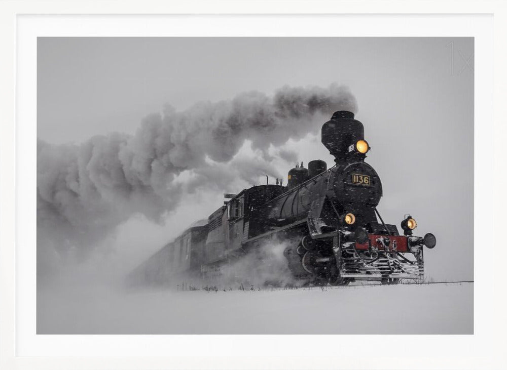 A dramatic black and white photograph of a classic steam train, number 1136, plowing through a heavy snowstorm, with its headlights glowing and a large plume of smoke trailing behind it. The image is presented within a silver frame. Print