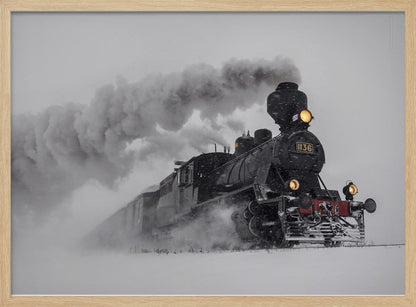 A dramatic black and white photograph of a classic steam train, number 1136, plowing through a heavy snowstorm, with its headlights glowing and a large plume of smoke trailing behind it. The image is presented within a silver frame. Print