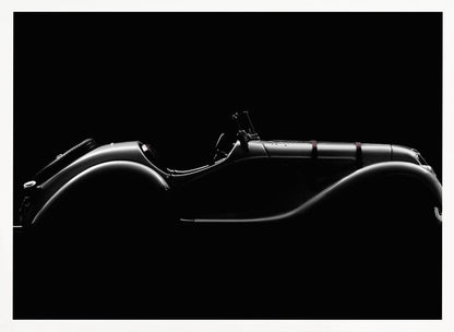 A dramatic black and white photograph showcasing the elegant silhouette of a vintage roadster. The side profile of the classic car is highlighted by subtle light, emphasizing its long hood and sweeping fenders against a solid black background, all within a brushed silver frame. Print