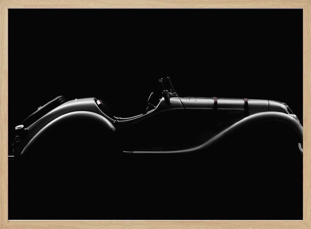 A dramatic black and white photograph showcasing the elegant silhouette of a vintage roadster. The side profile of the classic car is highlighted by subtle light, emphasizing its long hood and sweeping fenders against a solid black background, all within a brushed silver frame. Print