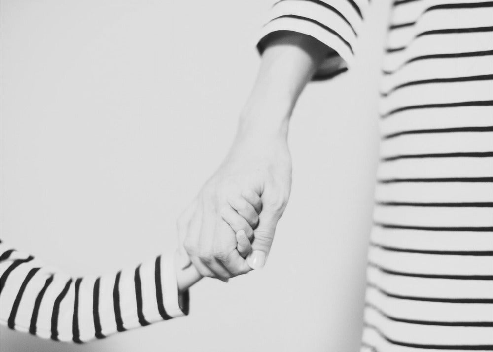 A tender black and white photograph capturing a close-up of a parent and child holding hands. Both are wearing matching striped shirts, emphasizing their connection. The image is presented in a silver frame. Print