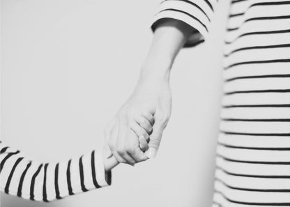 A tender black and white photograph capturing a close-up of a parent and child holding hands. Both are wearing matching striped shirts, emphasizing their connection. The image is presented in a silver frame. Print