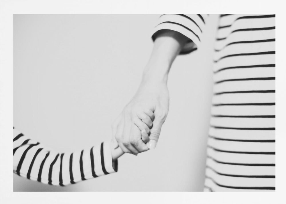 A tender black and white photograph capturing a close-up of a parent and child holding hands. Both are wearing matching striped shirts, emphasizing their connection. The image is presented in a silver frame. Print