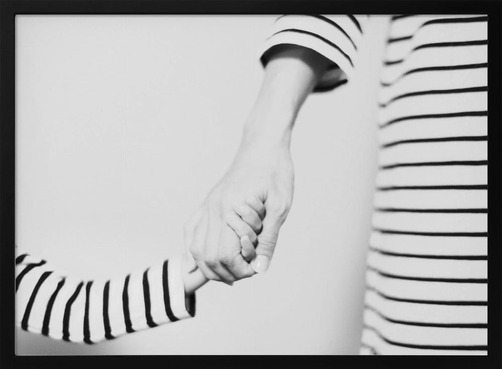 A tender black and white photograph capturing a close-up of a parent and child holding hands. Both are wearing matching striped shirts, emphasizing their connection. The image is presented in a silver frame. Print