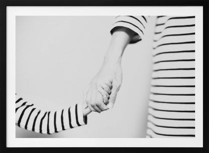 A tender black and white photograph capturing a close-up of a parent and child holding hands. Both are wearing matching striped shirts, emphasizing their connection. The image is presented in a silver frame. Print