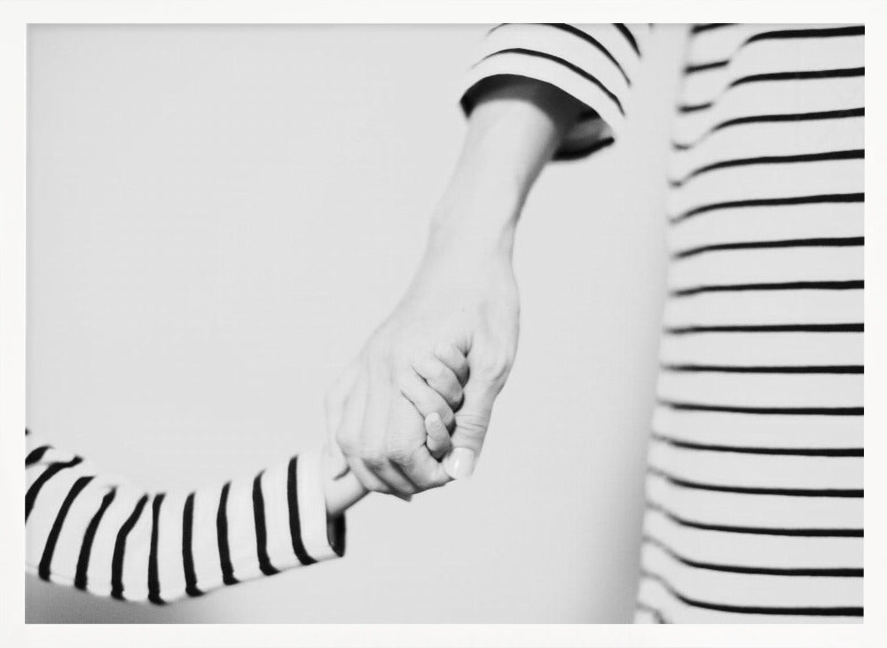 A tender black and white photograph capturing a close-up of a parent and child holding hands. Both are wearing matching striped shirts, emphasizing their connection. The image is presented in a silver frame. Print