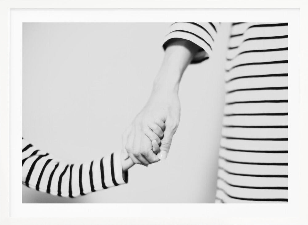 A tender black and white photograph capturing a close-up of a parent and child holding hands. Both are wearing matching striped shirts, emphasizing their connection. The image is presented in a silver frame. Print