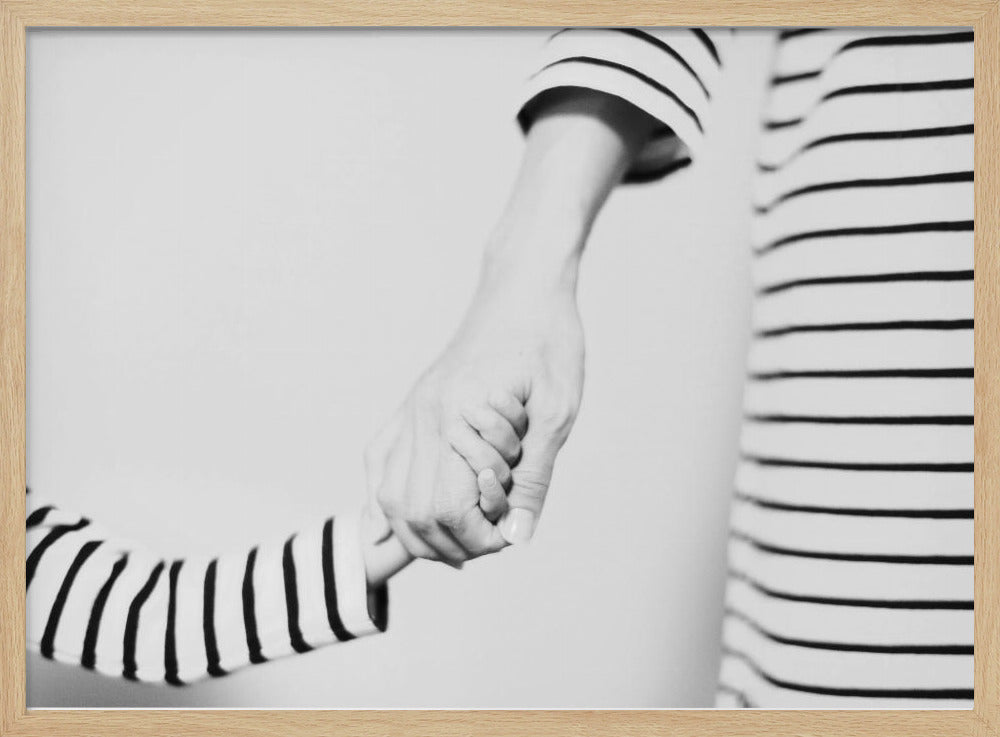 A tender black and white photograph capturing a close-up of a parent and child holding hands. Both are wearing matching striped shirts, emphasizing their connection. The image is presented in a silver frame. Print