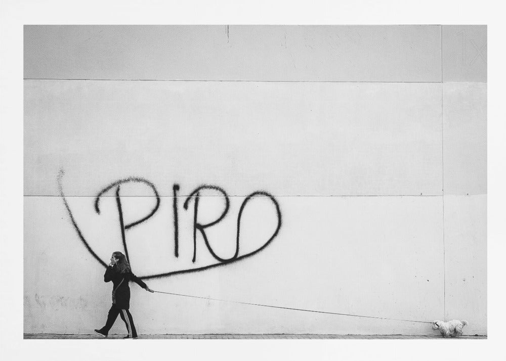 A minimalist black and white photograph of a woman dressed in black walking a small, fluffy white dog on a long leash. They are walking along a sidewalk in front of a large, pale wall with the word 'PIRO' written in black spray paint graffiti. The entire image is enclosed in a light grey frame. Poster
