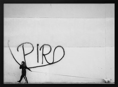 A minimalist black and white photograph of a woman dressed in black walking a small, fluffy white dog on a long leash. They are walking along a sidewalk in front of a large, pale wall with the word 'PIRO' written in black spray paint graffiti. The entire image is enclosed in a light grey frame. Poster