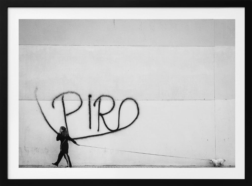 A minimalist black and white photograph of a woman dressed in black walking a small, fluffy white dog on a long leash. They are walking along a sidewalk in front of a large, pale wall with the word 'PIRO' written in black spray paint graffiti. The entire image is enclosed in a light grey frame. Poster
