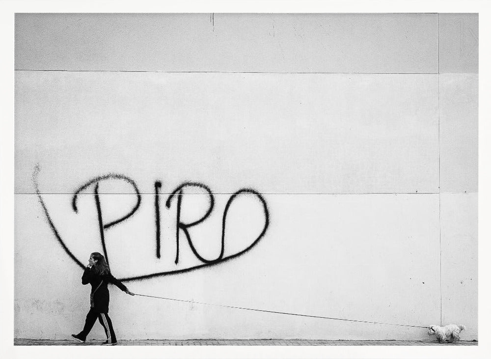 A minimalist black and white photograph of a woman dressed in black walking a small, fluffy white dog on a long leash. They are walking along a sidewalk in front of a large, pale wall with the word 'PIRO' written in black spray paint graffiti. The entire image is enclosed in a light grey frame. Poster