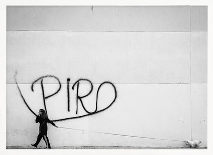A minimalist black and white photograph of a woman dressed in black walking a small, fluffy white dog on a long leash. They are walking along a sidewalk in front of a large, pale wall with the word 'PIRO' written in black spray paint graffiti. The entire image is enclosed in a light grey frame. Poster