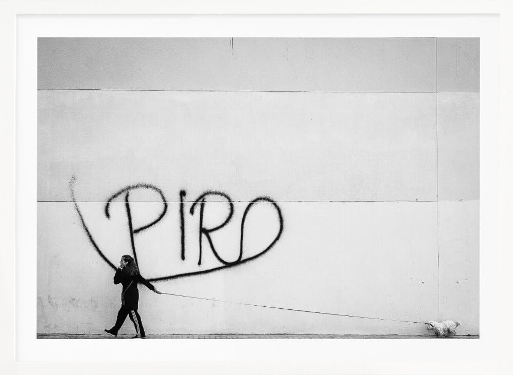 A minimalist black and white photograph of a woman dressed in black walking a small, fluffy white dog on a long leash. They are walking along a sidewalk in front of a large, pale wall with the word 'PIRO' written in black spray paint graffiti. The entire image is enclosed in a light grey frame. Poster