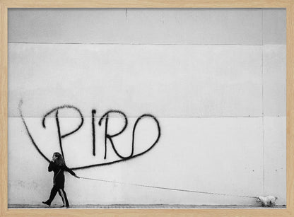 A minimalist black and white photograph of a woman dressed in black walking a small, fluffy white dog on a long leash. They are walking along a sidewalk in front of a large, pale wall with the word 'PIRO' written in black spray paint graffiti. The entire image is enclosed in a light grey frame. Poster