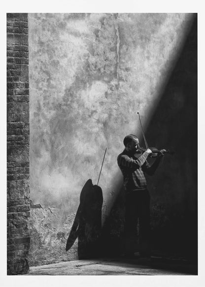 A dramatic black and white photograph of a man playing the violin, standing in a corner against a weathered wall. He is bathed in a sharp diagonal ray of light, casting a long, dark shadow behind him. Artwork