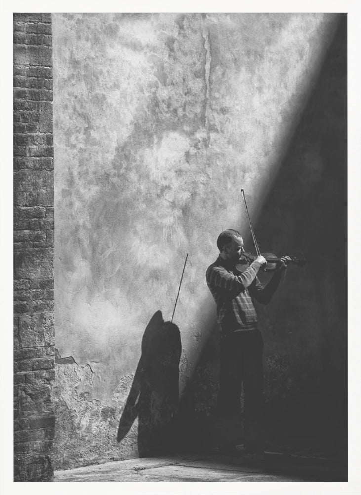 A dramatic black and white photograph of a man playing the violin, standing in a corner against a weathered wall. He is bathed in a sharp diagonal ray of light, casting a long, dark shadow behind him. Artwork