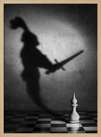A black and white conceptual photograph of a single white chess piece on a checkerboard, casting a large, ominous shadow of a medieval knight holding a sword against a textured wall. Print