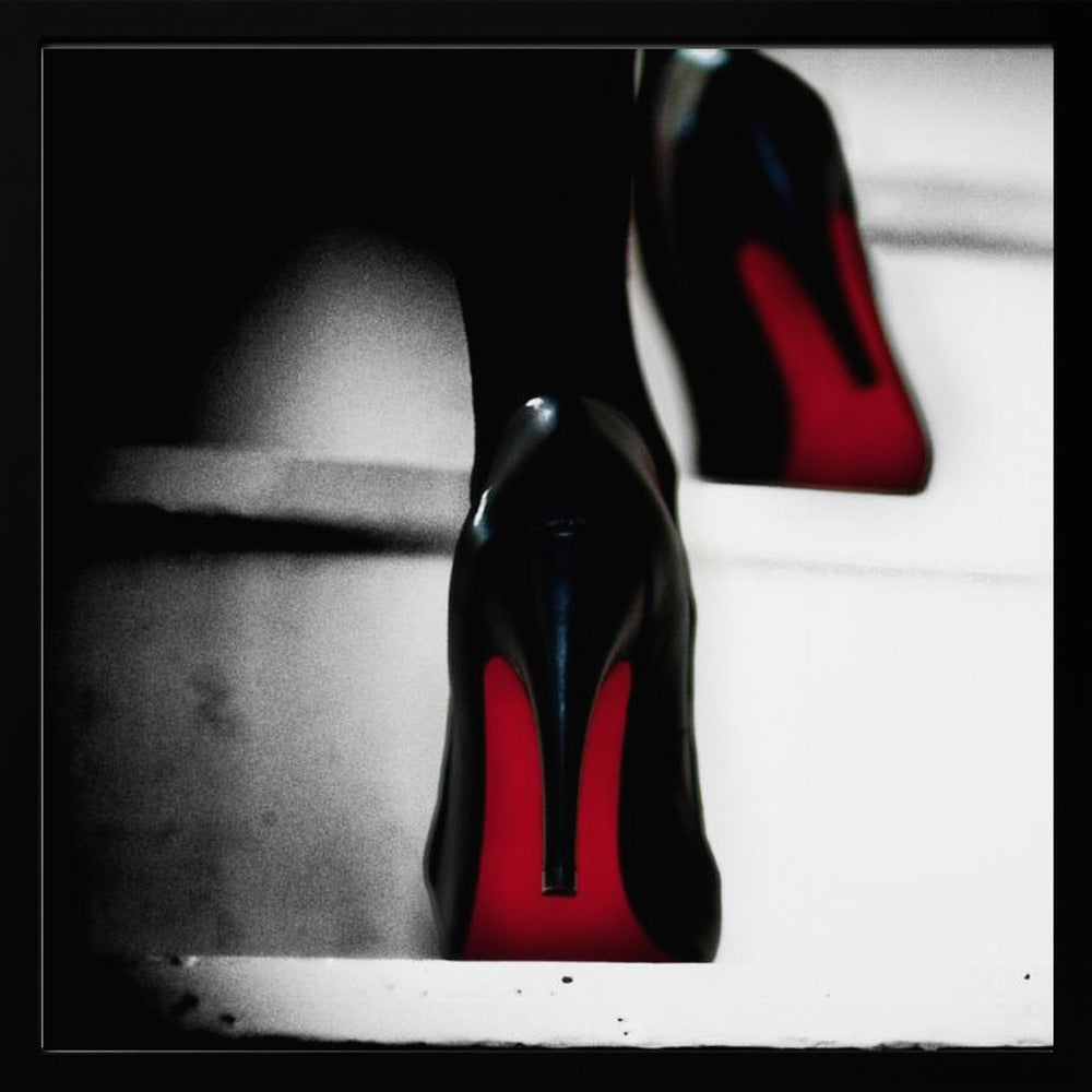 A dramatic, low-angle, black and white photograph focusing on the back of a person wearing glossy black high heels with vibrant red soles, all set within a light wood frame. Artwork