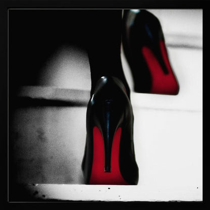 A dramatic, low-angle, black and white photograph focusing on the back of a person wearing glossy black high heels with vibrant red soles, all set within a light wood frame. Artwork