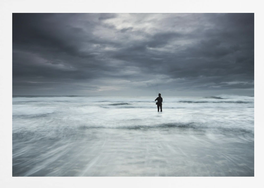 A moody, long-exposure photograph of a silhouetted fisherman standing in the churning white surf of the ocean under a dark, stormy sky, presented in a silver frame. Wall Art