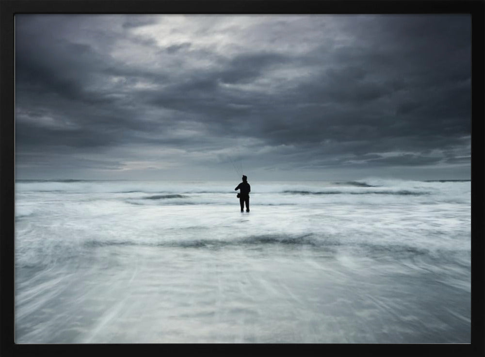 A moody, long-exposure photograph of a silhouetted fisherman standing in the churning white surf of the ocean under a dark, stormy sky, presented in a silver frame. Wall Art