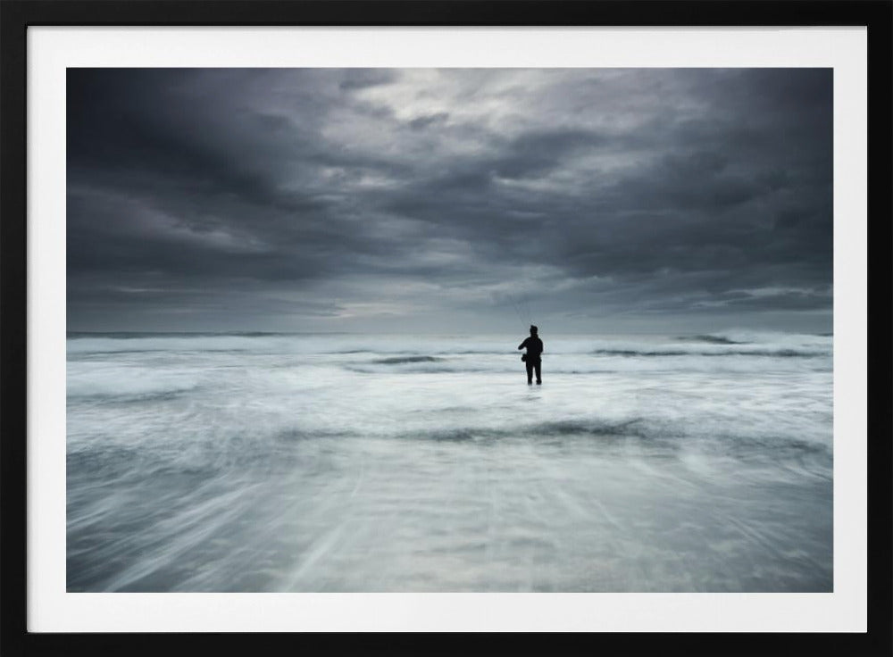 A moody, long-exposure photograph of a silhouetted fisherman standing in the churning white surf of the ocean under a dark, stormy sky, presented in a silver frame. Wall Art