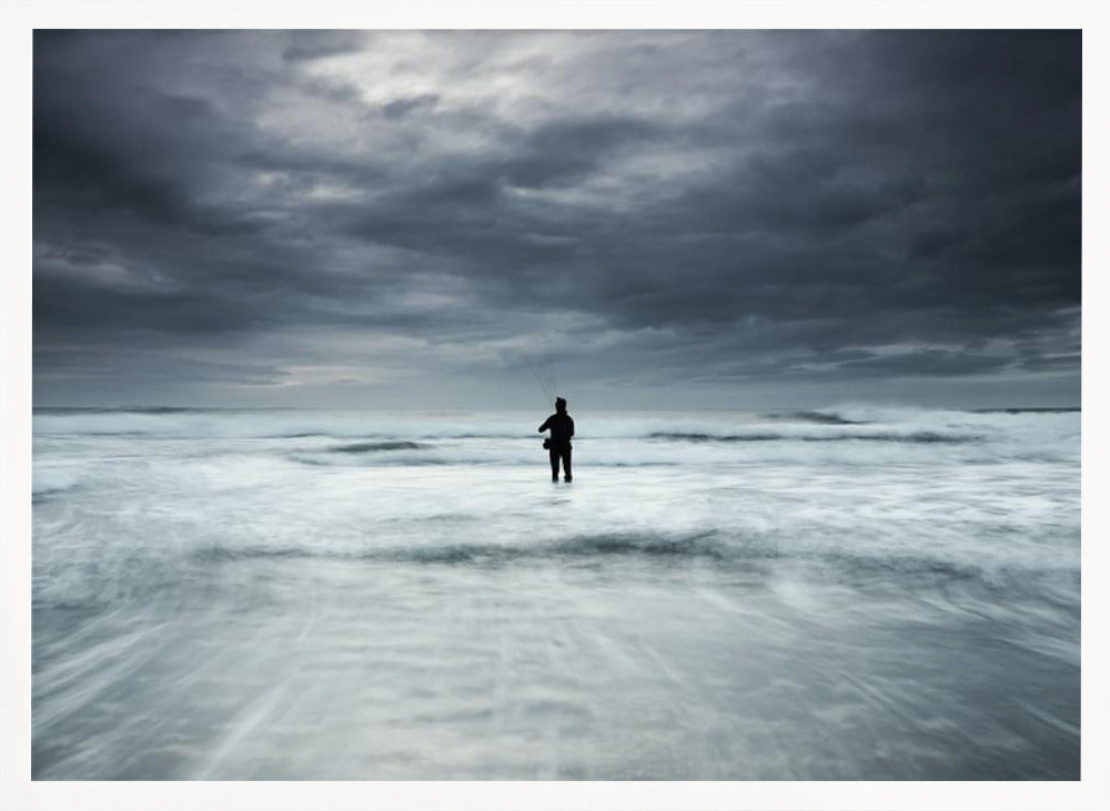 A moody, long-exposure photograph of a silhouetted fisherman standing in the churning white surf of the ocean under a dark, stormy sky, presented in a silver frame. Wall Art