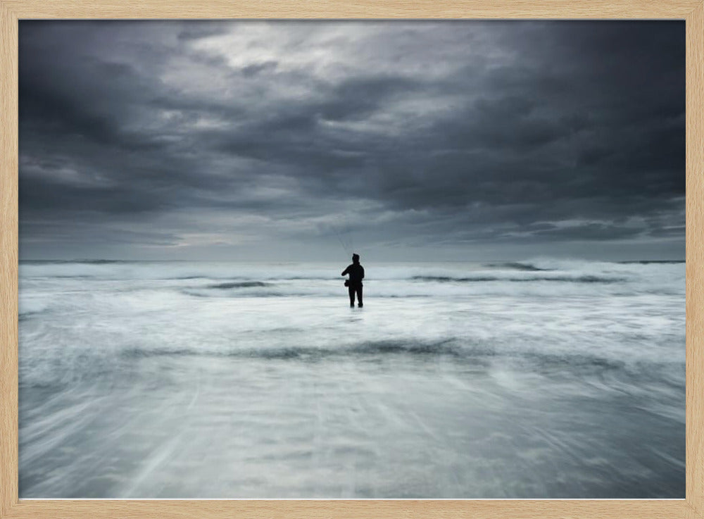 A moody, long-exposure photograph of a silhouetted fisherman standing in the churning white surf of the ocean under a dark, stormy sky, presented in a silver frame. Wall Art