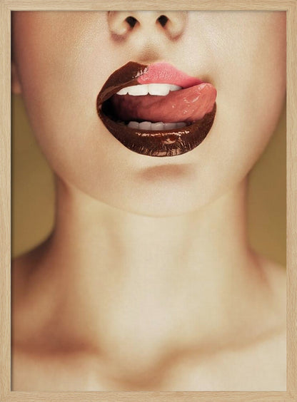 A close-up photograph of a woman's mouth with two-toned lipstick. The lips are mostly covered in glossy dark brown, with the upper right section in light pink. Her tongue is out, licking the pink part of her lip, revealing her white teeth. Print