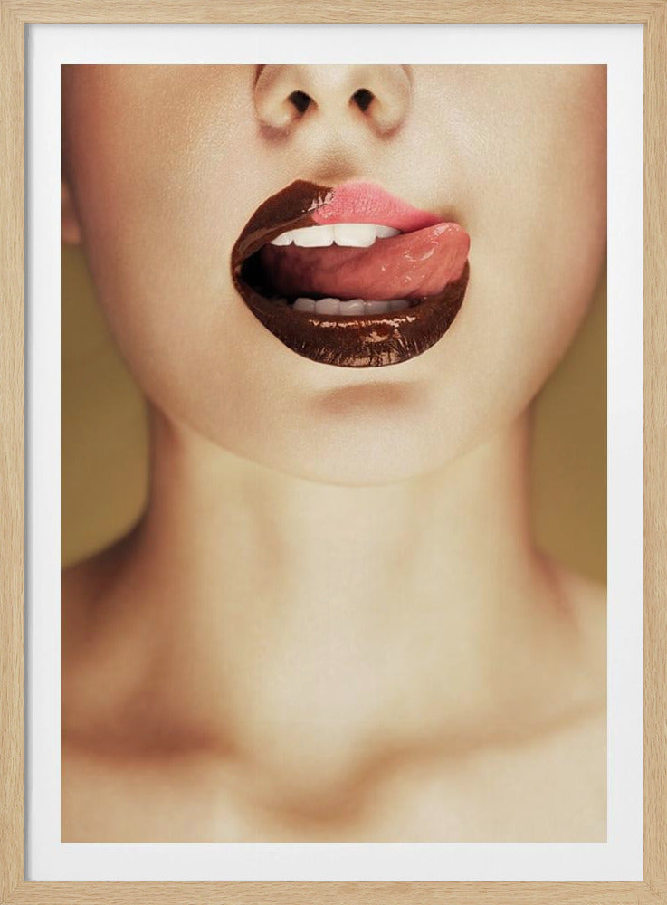 A close-up photograph of a woman's mouth with two-toned lipstick. The lips are mostly covered in glossy dark brown, with the upper right section in light pink. Her tongue is out, licking the pink part of her lip, revealing her white teeth. Print
