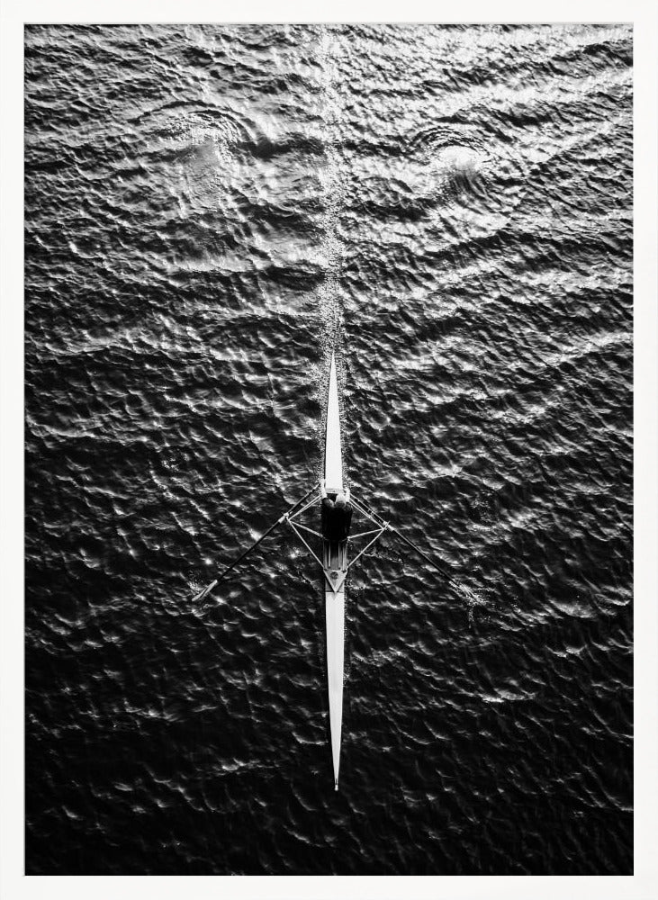 A dramatic black and white overhead photograph of a lone rower in a sleek racing shell, cutting a straight path through dark, textured water. The high-contrast lighting highlights the ripples on the water's surface and the rower's focused form. Artwork