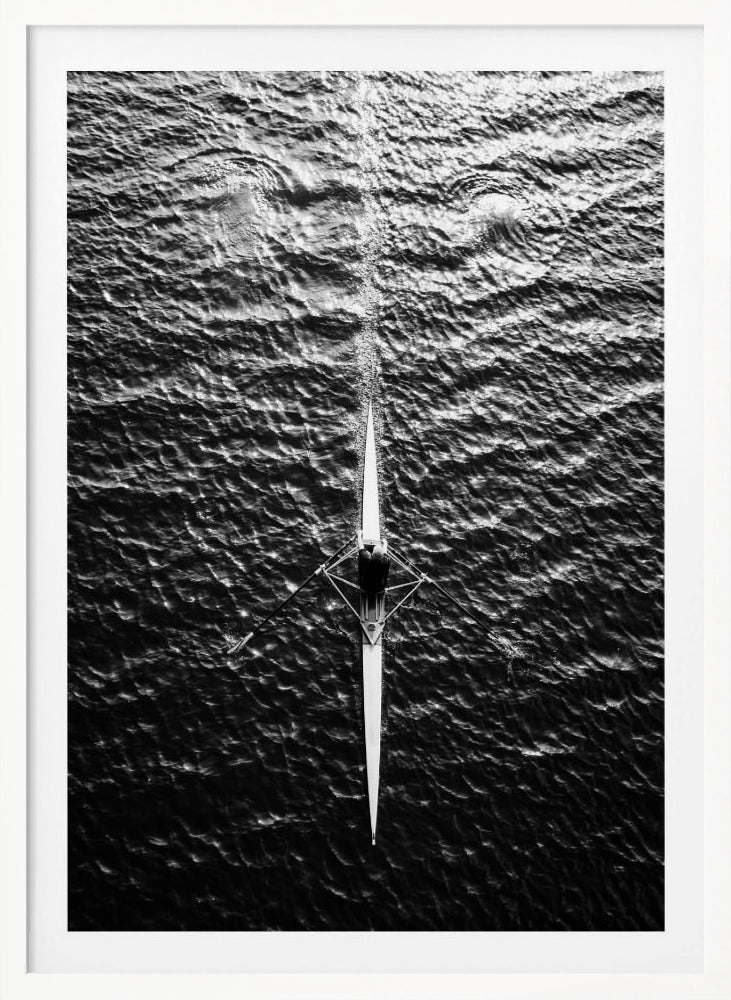 A dramatic black and white overhead photograph of a lone rower in a sleek racing shell, cutting a straight path through dark, textured water. The high-contrast lighting highlights the ripples on the water's surface and the rower's focused form. Artwork