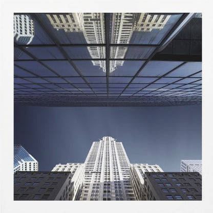 A framed, low-angle photograph capturing a stark white skyscraper against a deep blue sky, with its perfect reflection mirrored in the dark glass facade of an overhanging building, creating a surreal and symmetrical composition. Wall Art