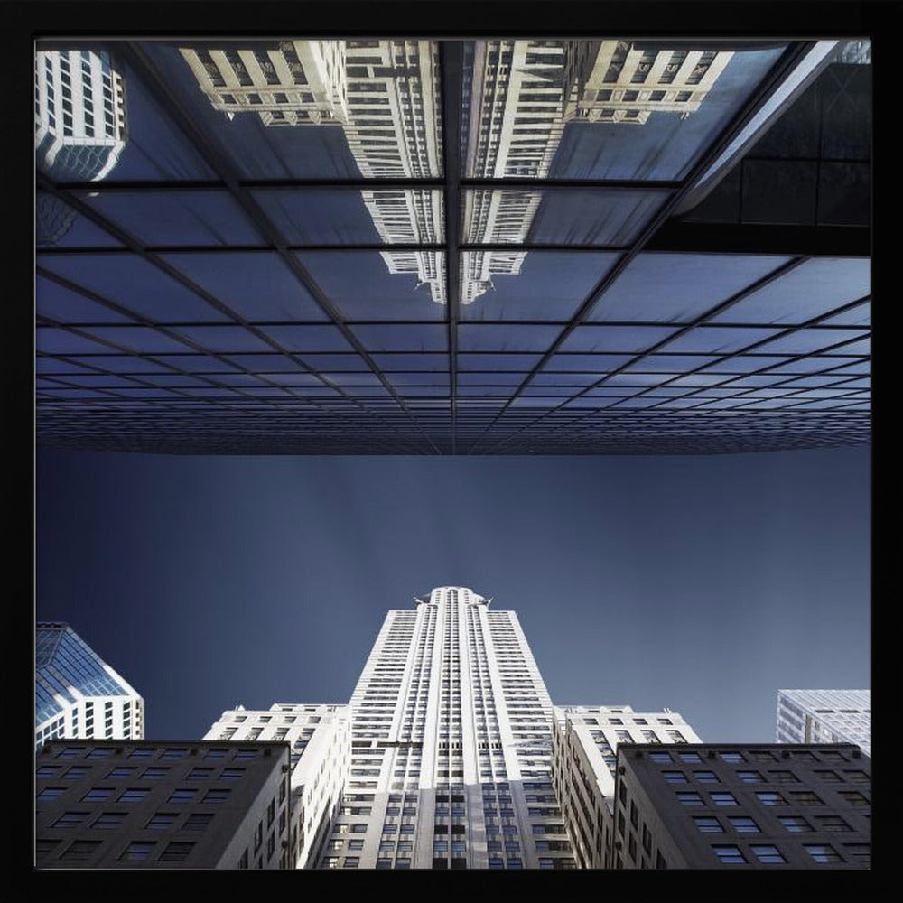 A framed, low-angle photograph capturing a stark white skyscraper against a deep blue sky, with its perfect reflection mirrored in the dark glass facade of an overhanging building, creating a surreal and symmetrical composition. Wall Art