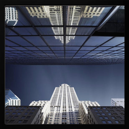 A framed, low-angle photograph capturing a stark white skyscraper against a deep blue sky, with its perfect reflection mirrored in the dark glass facade of an overhanging building, creating a surreal and symmetrical composition. Wall Art