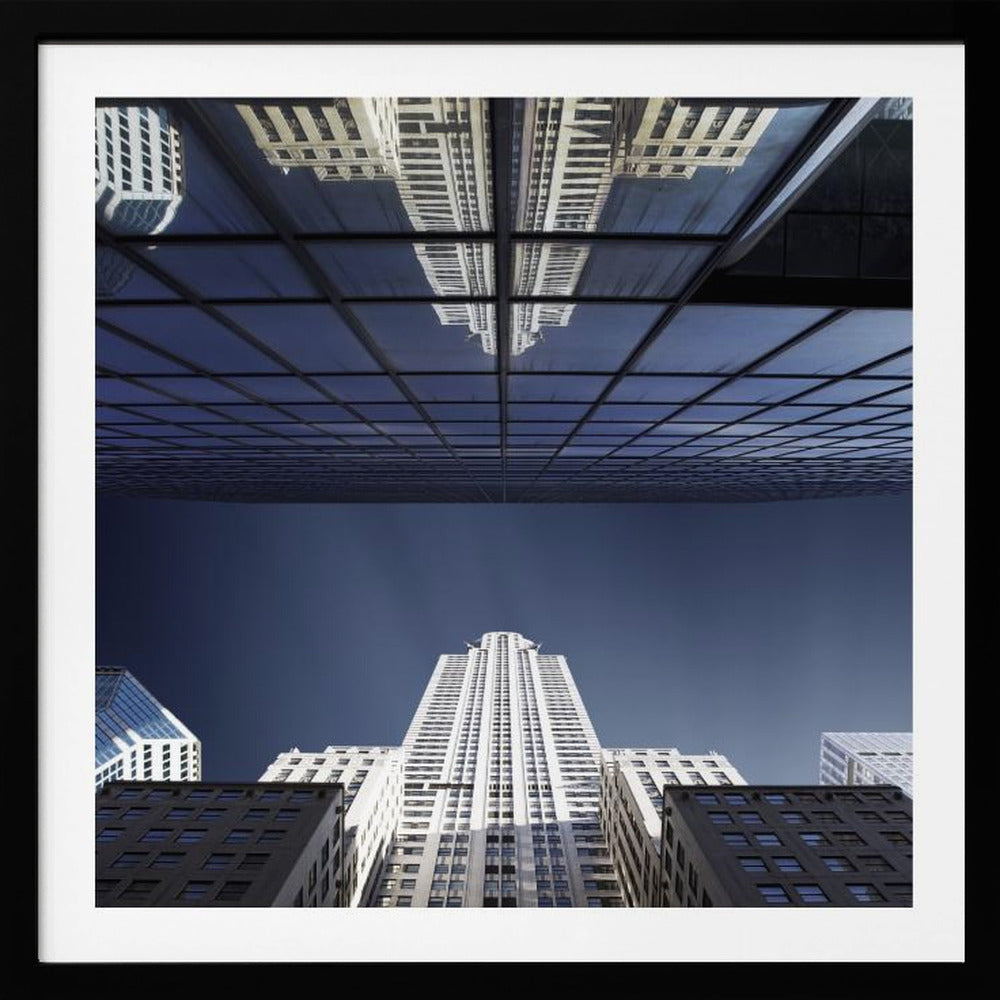 A framed, low-angle photograph capturing a stark white skyscraper against a deep blue sky, with its perfect reflection mirrored in the dark glass facade of an overhanging building, creating a surreal and symmetrical composition. Wall Art