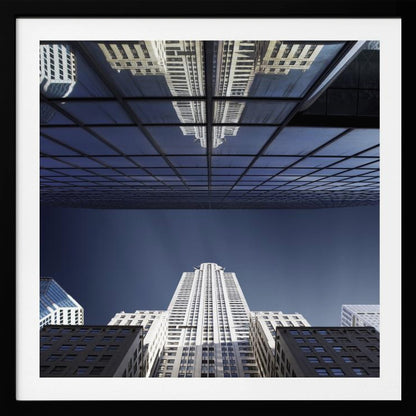 A framed, low-angle photograph capturing a stark white skyscraper against a deep blue sky, with its perfect reflection mirrored in the dark glass facade of an overhanging building, creating a surreal and symmetrical composition. Wall Art